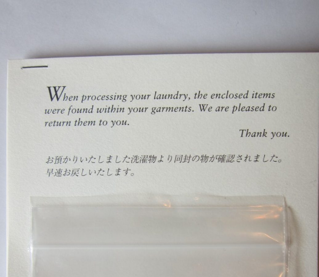 A letterpress card found folded in returned laundry: “When processing your laundry, the enclosed items were found within your garments. We are pleased to return them to you. Thank you.”, repeated in Japanese, with the items sealed in a small bag