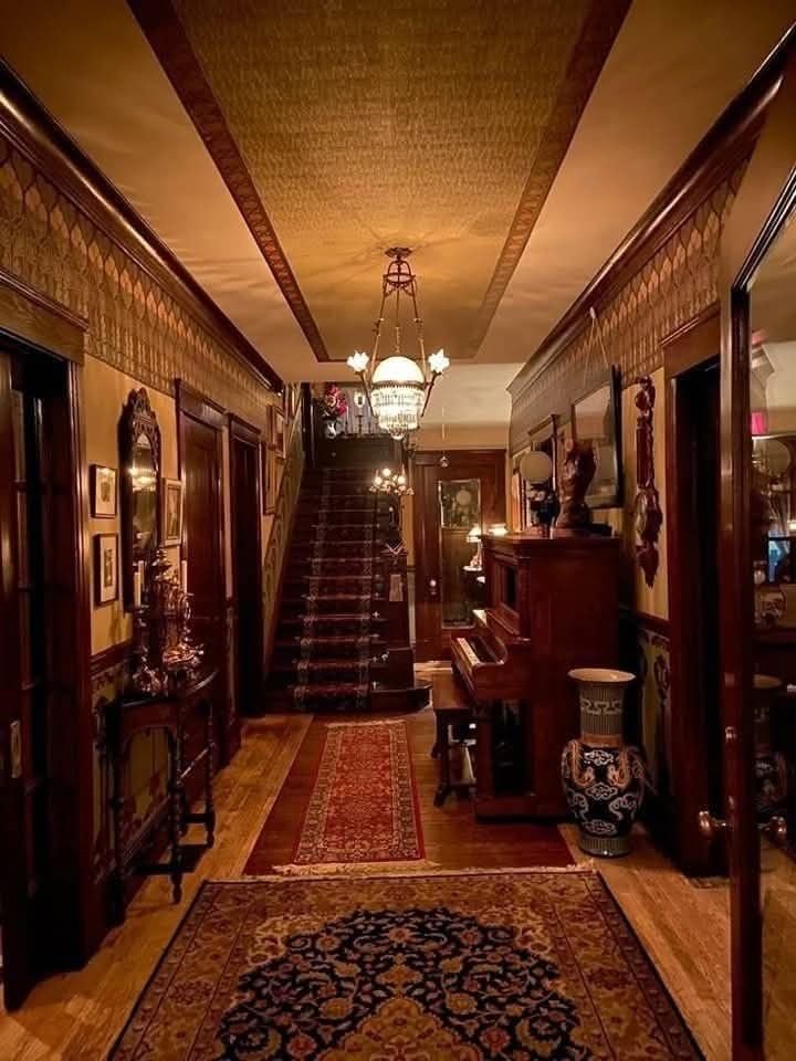 A panelled hallway with a chandelier, staircase and patterned runner