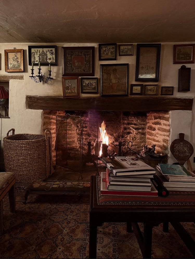 A rustic room with a lit fire and framed pictures crowding a whitewashed wall
