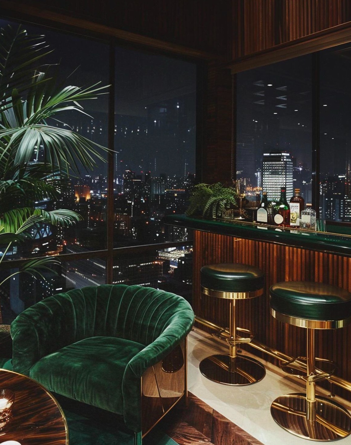 A green velvet bar with brass stools, overlooking a city at night