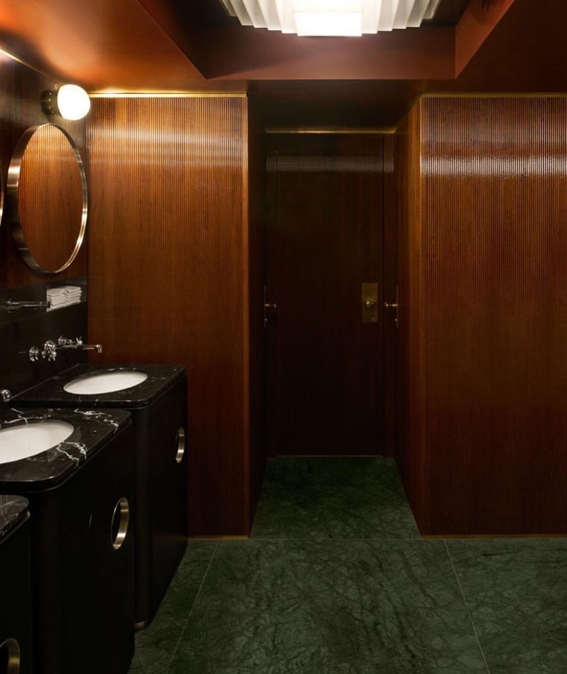 A wood-panelled washroom with a round mirror and dark stone
