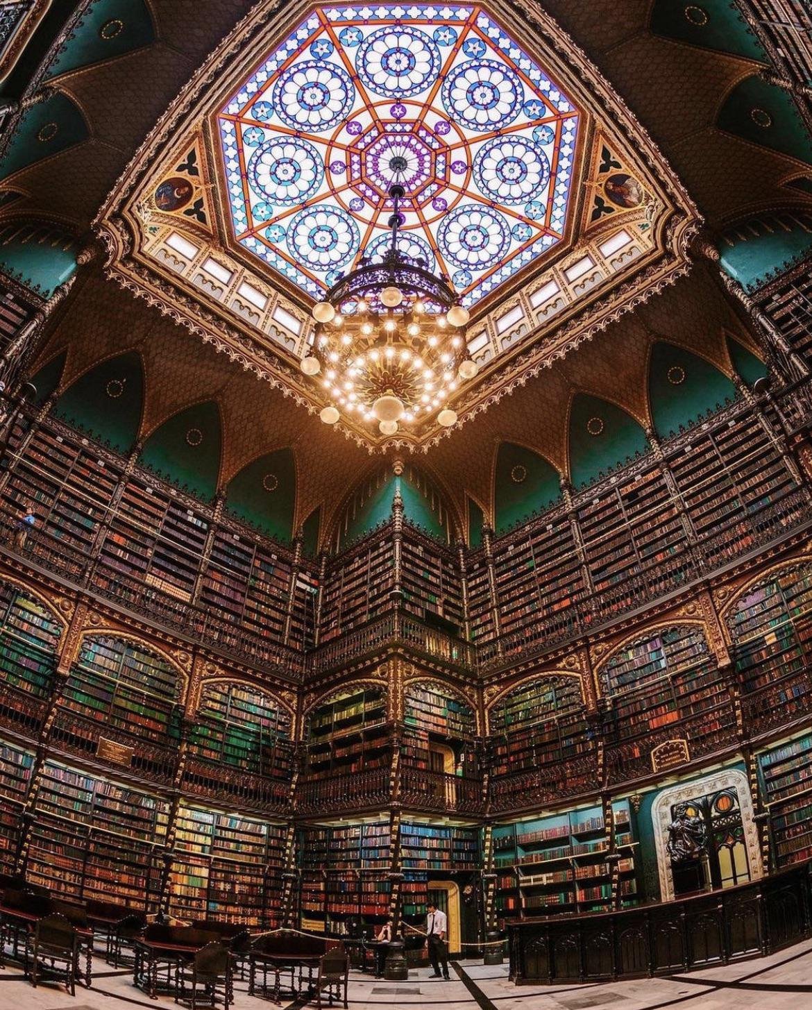 A domed library of tiered bookshelves beneath a stained-glass ceiling